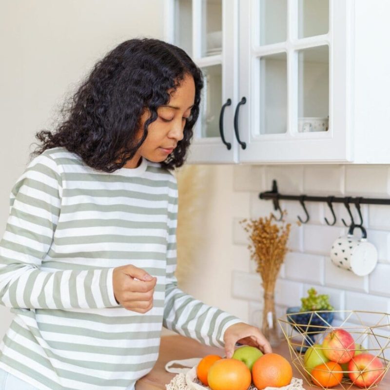 Female African-American woman taking out fruit bought at grocery store. Using eco-bags for shopping trips. Concept of healthy food and eco-friendly sustainable lifestyle